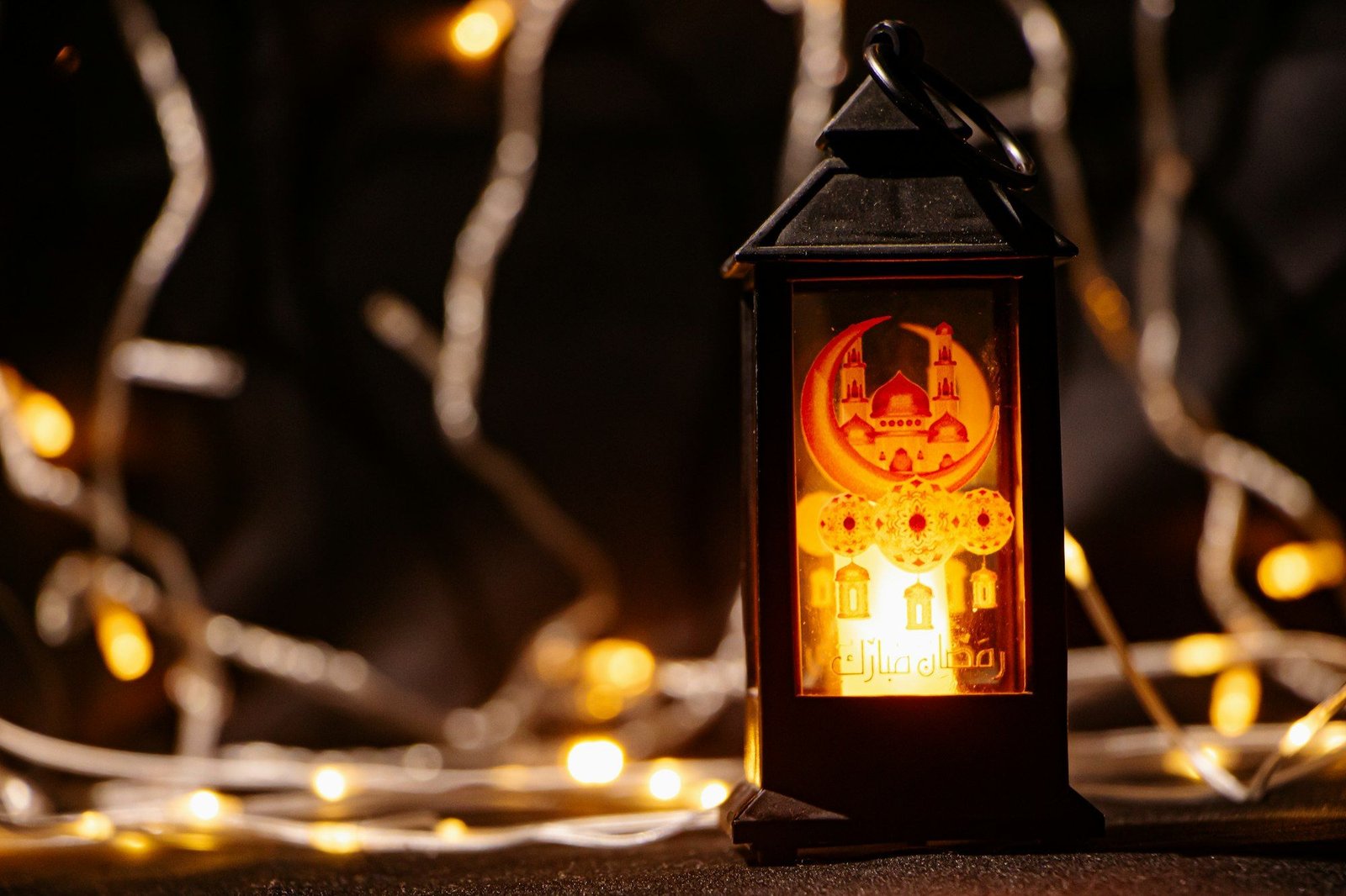 A lit Ramadan lantern with festive lights in the background