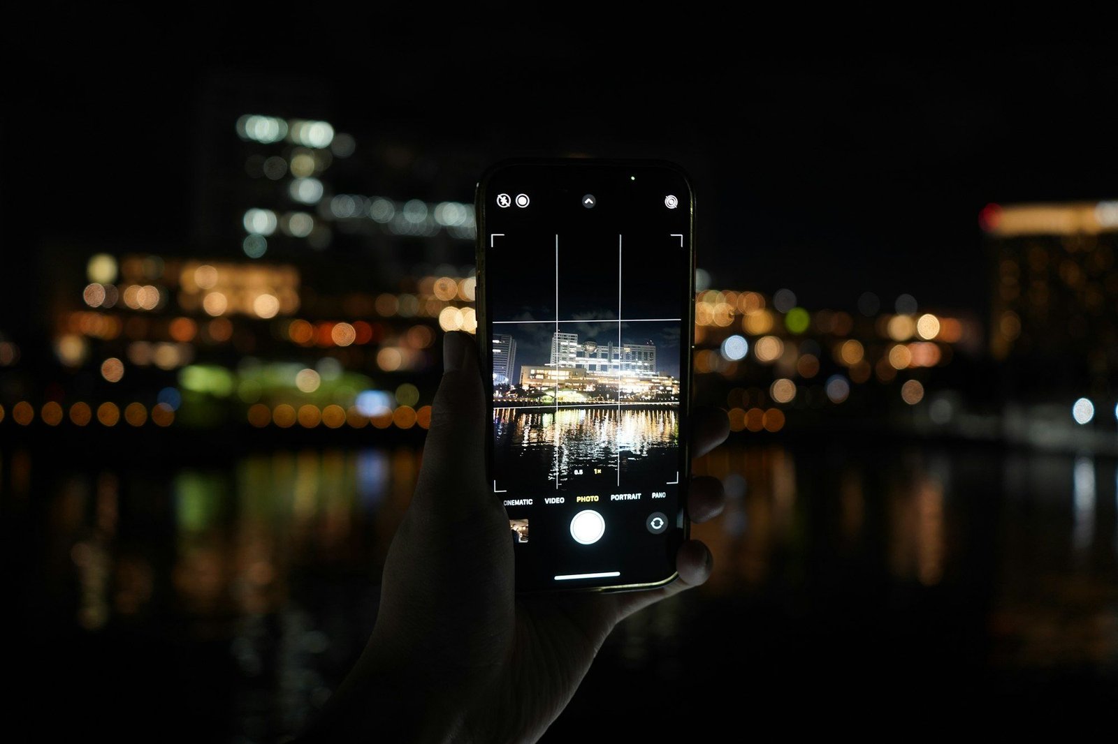 Hand holding a phone capturing city lights at night