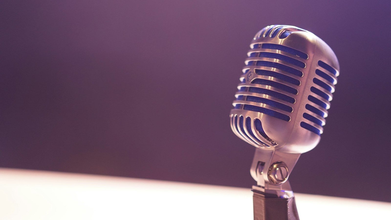 A vintage silver microphone against a soft purple background