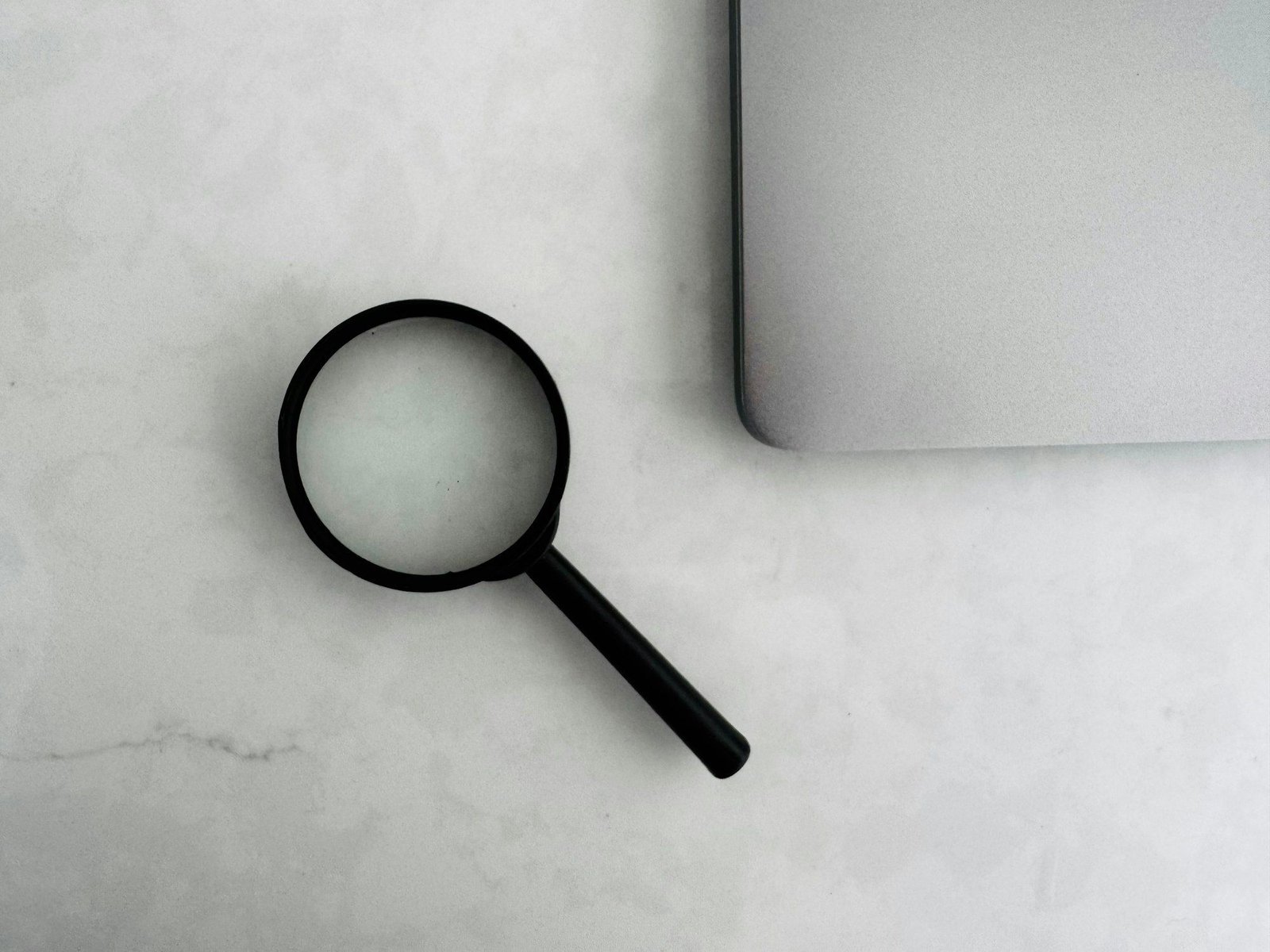 A magnifying glass next to a laptop on a marble table