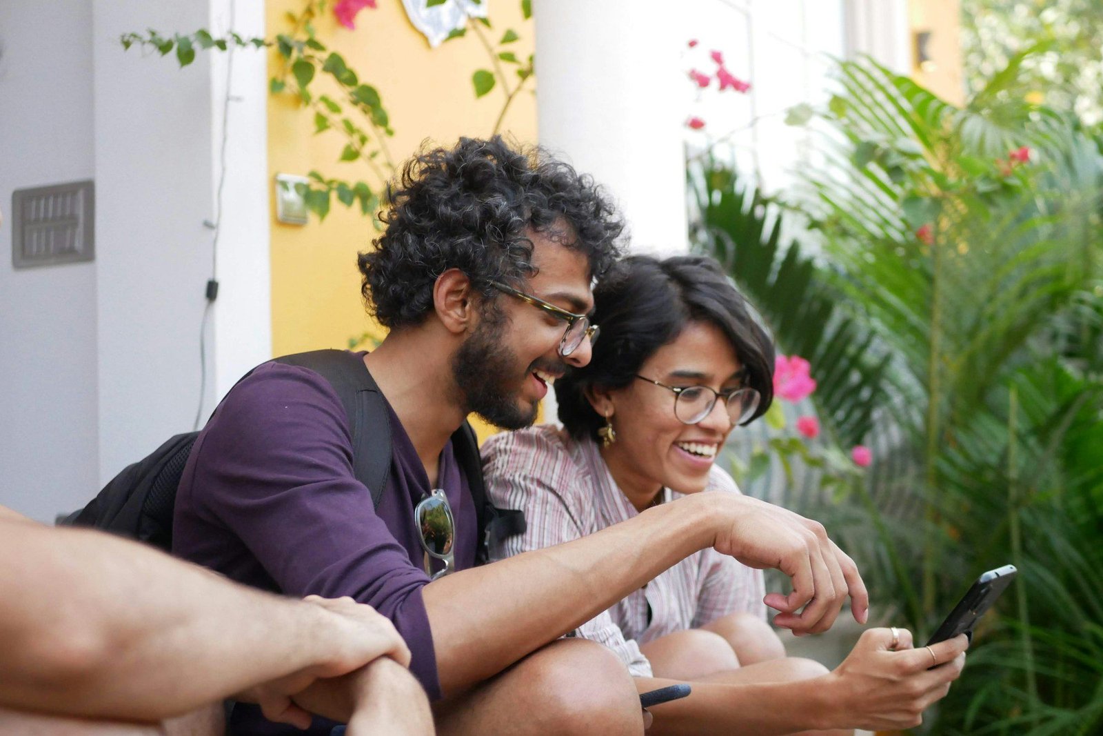A man and a woman laughing while looking at a smartphone outdoors
