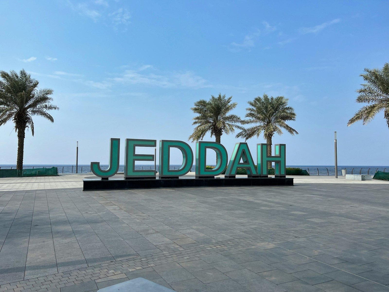 A large sign that says Jeddah in front of palm trees
