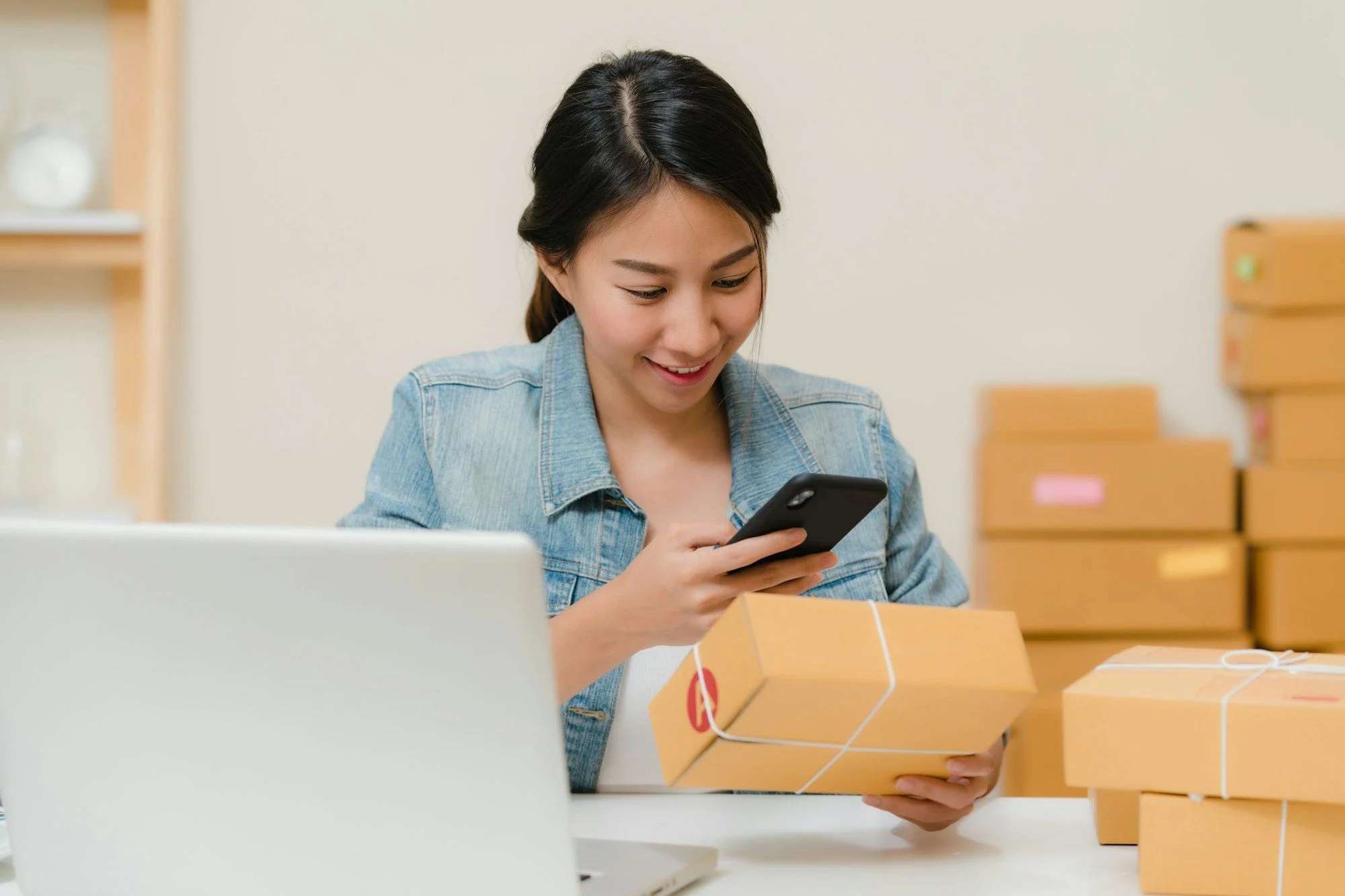 A woman checks a delivery package on her phone beside a laptop, an ecommerce SEO scene